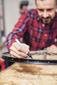 man leaning on bicycle rim and making a mark with a permanent marker